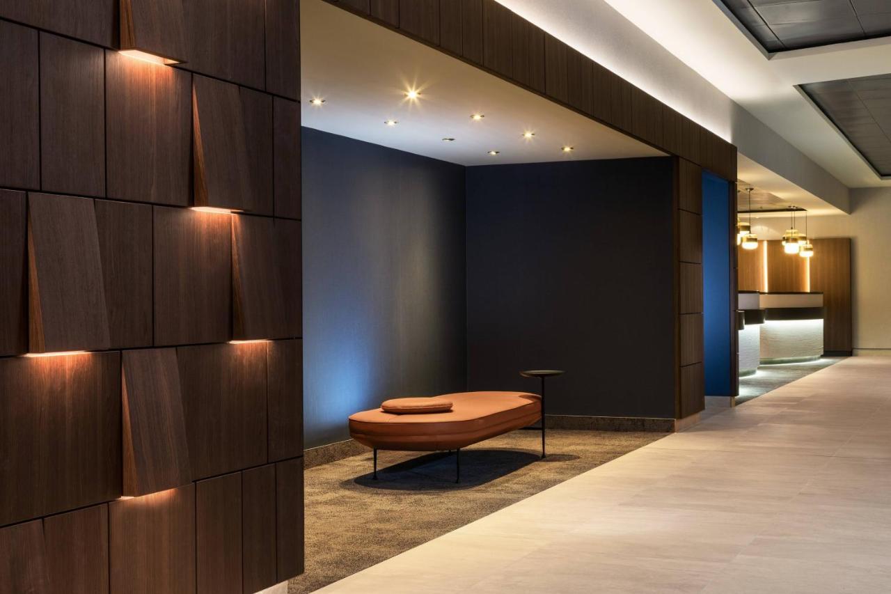Frankfurt Airport Marriott Hotel فرانكفورت المظهر الخارجي الصورة The photo shows a modern interior space characterized by a minimalist design. On one side, there is a wall with wooden panels that feature a textured pattern. The wall is illuminated with soft lighting, creating a warm ambiance. In the center of the 