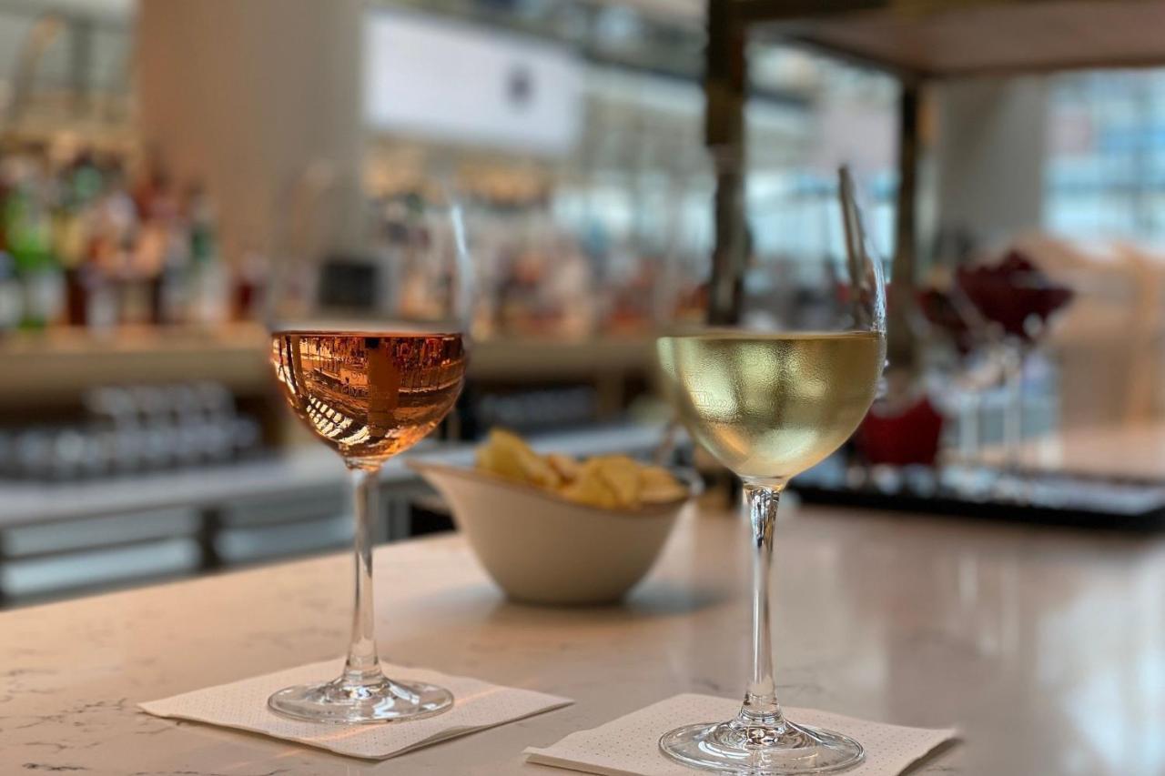 Frankfurt Airport Marriott Hotel فرانكفورت المظهر الخارجي الصورة The photo shows two glasses of wine placed on a marble countertop. On the left, there is a glass of rosé wine, and on the right, a glass of white wine. Both glasses are elegantly shaped and have a small square white napkin underneath them. In the bac