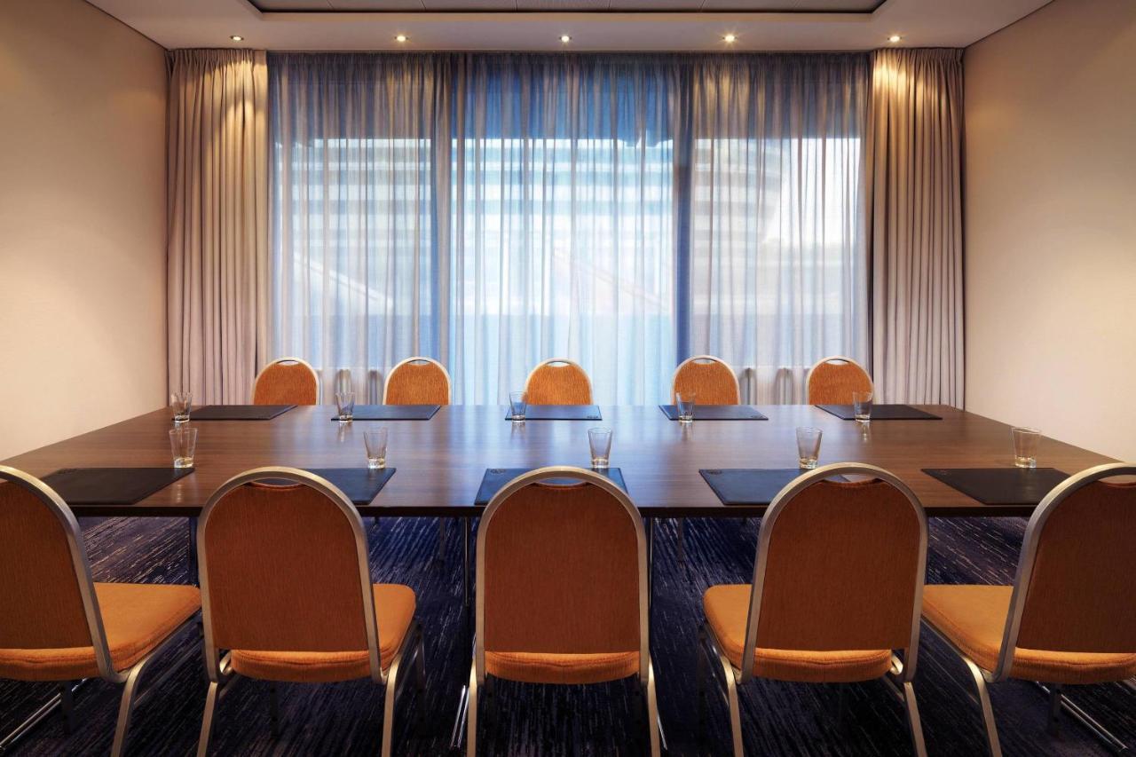Frankfurt Airport Marriott Hotel فرانكفورت المظهر الخارجي الصورة The photo depicts a meeting room featuring a long rectangular table surrounded by several chairs. The chairs are orange with a simple design. On the table, there are water glasses placed in front of each chair, indicating it's ready for a meeting or 
