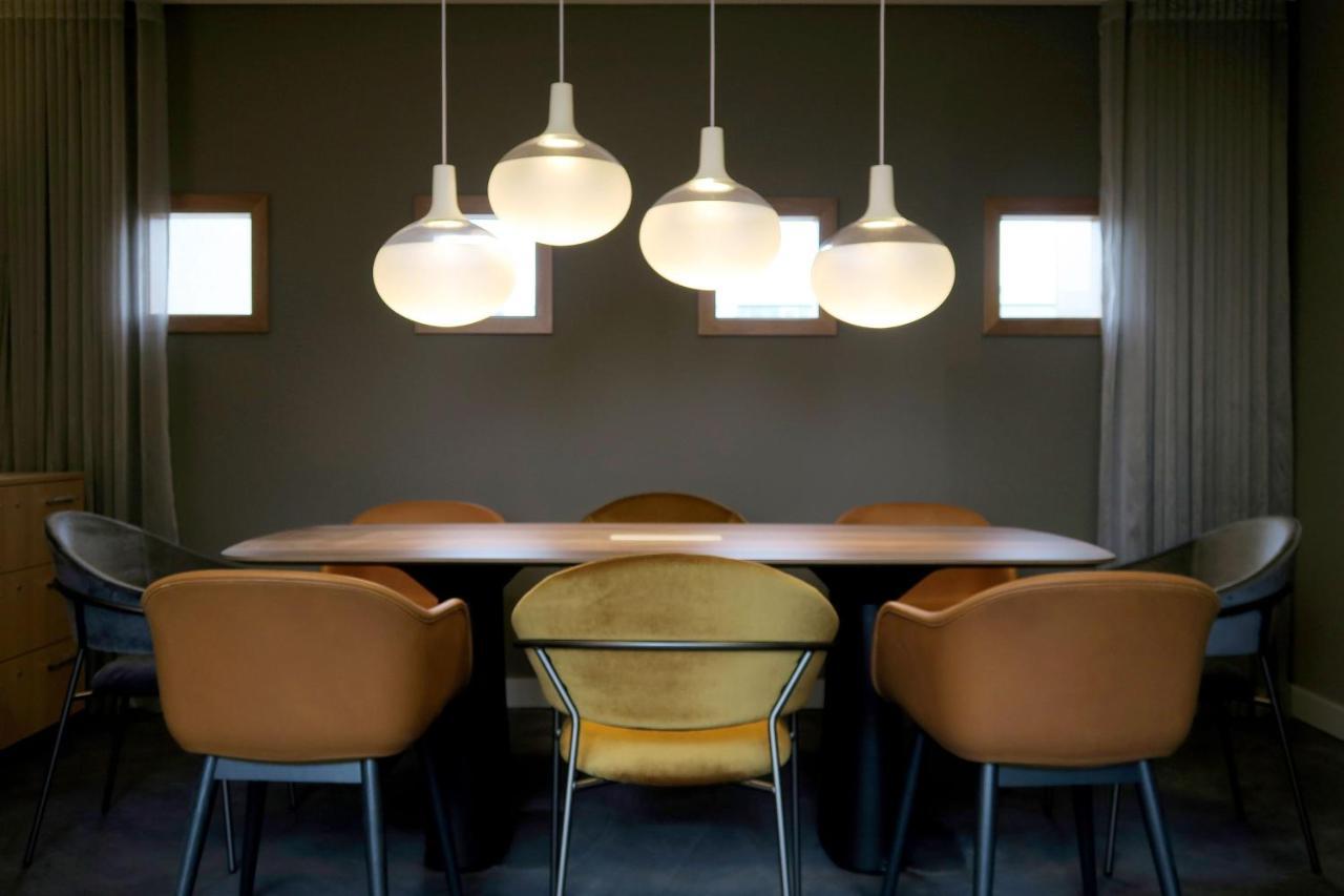 Frankfurt Airport Marriott Hotel فرانكفورت المظهر الخارجي الصورة The photo shows a modern dining area featuring a long table surrounded by several chairs. Above the table, there are four pendant lights with a sleek design that emit a warm glow. The walls are painted in a muted tone, and there are two small windows
