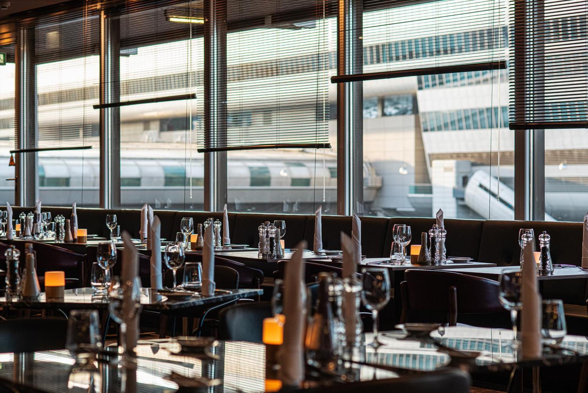 Frankfurt Airport Marriott Hotel فرانكفورت المظهر الخارجي الصورة The photo shows the interior of a restaurant with a modern design. The tables are elegantly set with glassware, folded napkins, and small candles, creating a sophisticated dining atmosphere. Large windows allow natural light to flood the space and pr