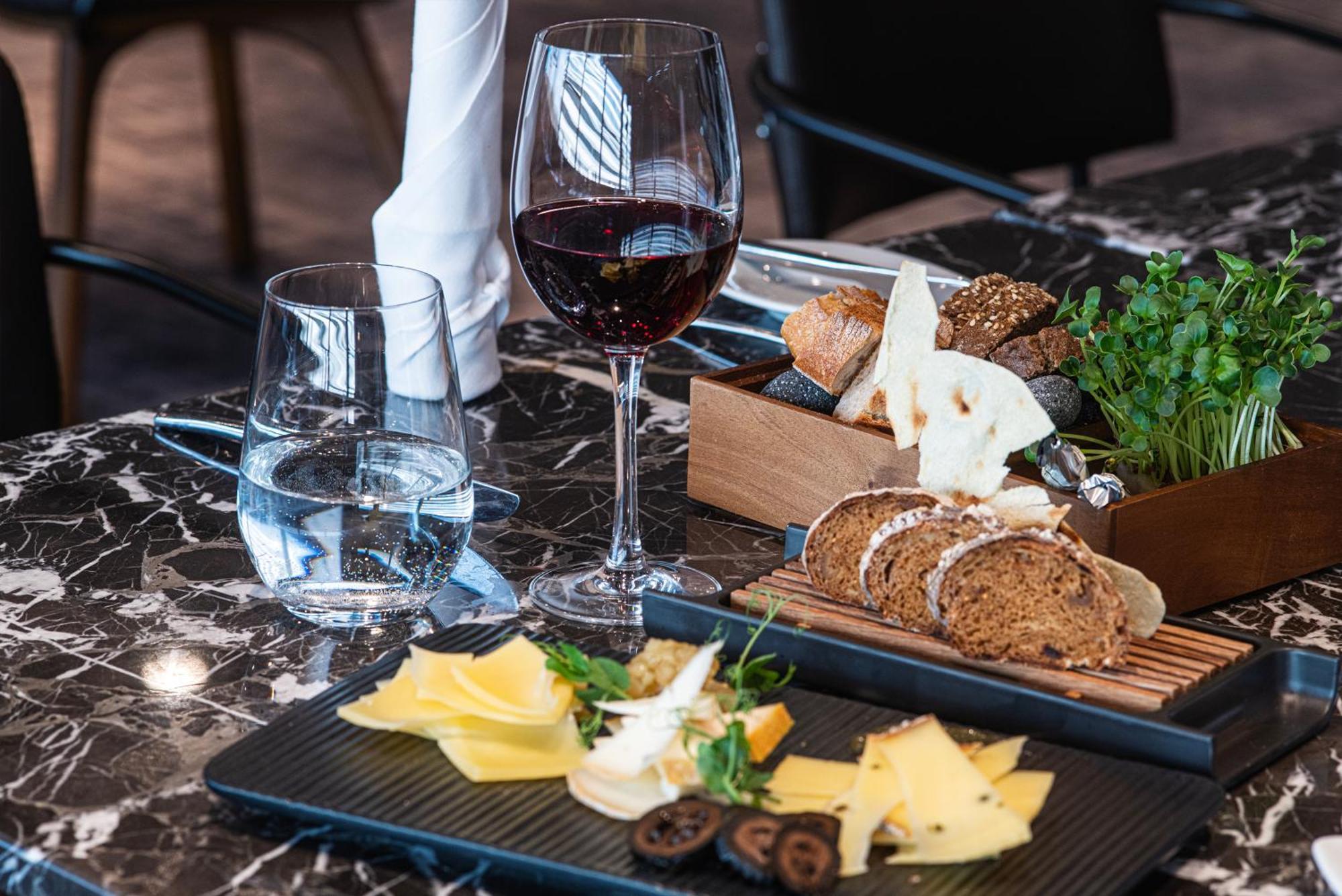 Frankfurt Airport Marriott Hotel فرانكفورت المظهر الخارجي الصورة The image shows a beautifully arranged dining table. There are two glasses: one containing red wine and the other with water. On the table, there is a selection of cheeses displayed on a black rectangular platter, accompanied by some herbs and dried 