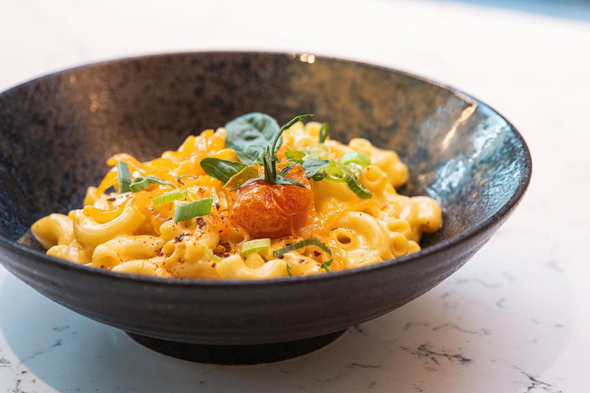 Frankfurt Airport Marriott Hotel فرانكفورت المظهر الخارجي الصورة The photo shows a bowl of macaroni and cheese. The dish features creamy, elbow macaroni coated in a cheesy sauce, topped with garnishes like green herbs, potentially some spice, and a piece of orange garnishment. The bowl is dark and round, placed on