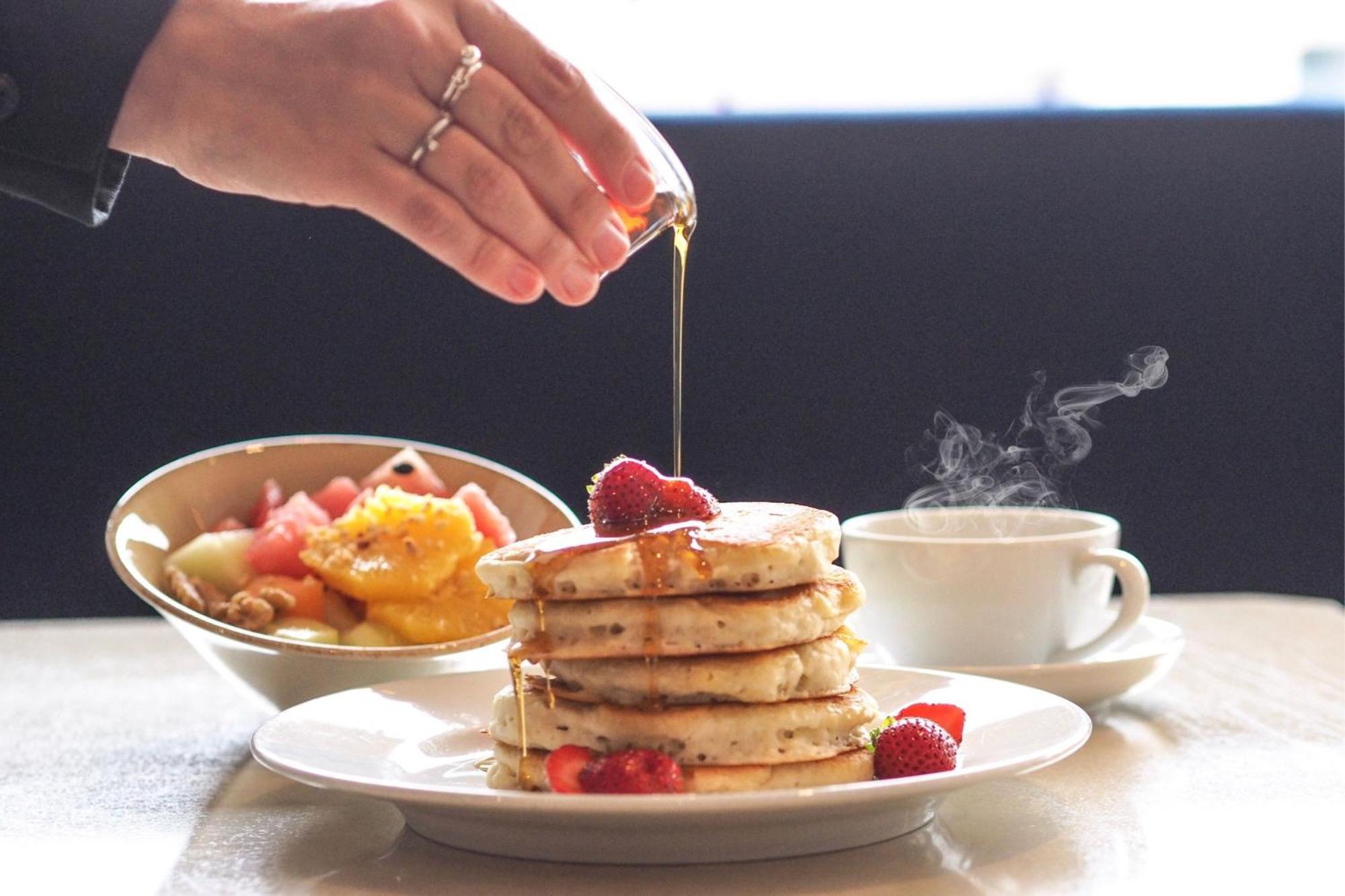 Frankfurt Airport Marriott Hotel فرانكفورت المظهر الخارجي الصورة The photo shows a delicious breakfast scene featuring a stack of pancakes drizzled with syrup. A hand is pouring syrup onto the pancakes. There are fresh strawberries on top of the stack as well. In the background, there's a bowl of mixed fruit, incl