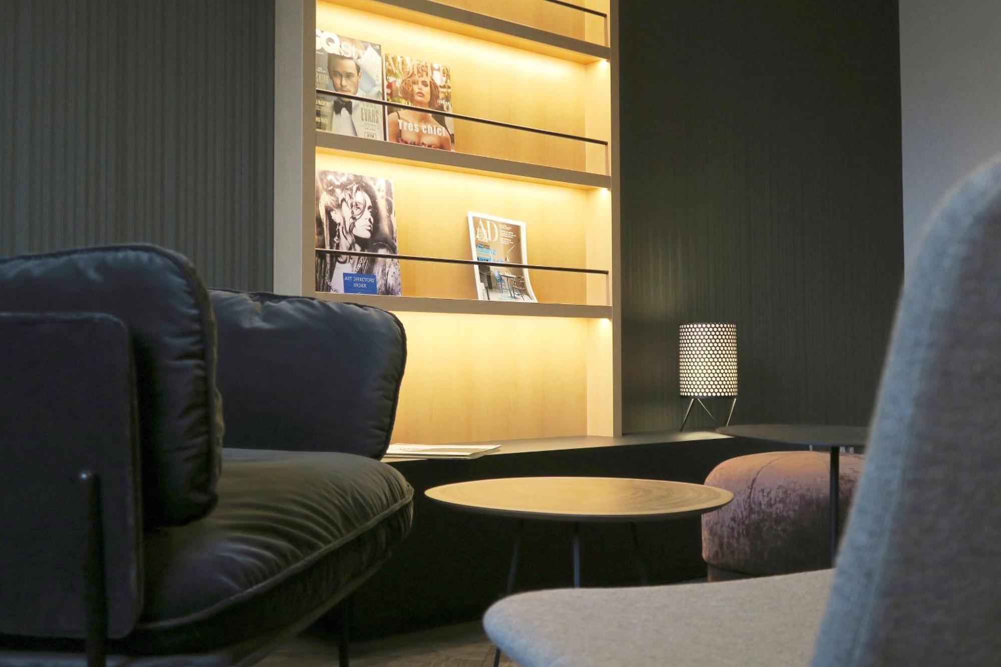 Frankfurt Airport Marriott Hotel فرانكفورت المظهر الخارجي الصورة The photo shows a modern interior space featuring a cozy seating arrangement. There are two types of chairs with soft cushions, positioned around a small round coffee table. In the background, there's a stylish shelving unit that displays several mag