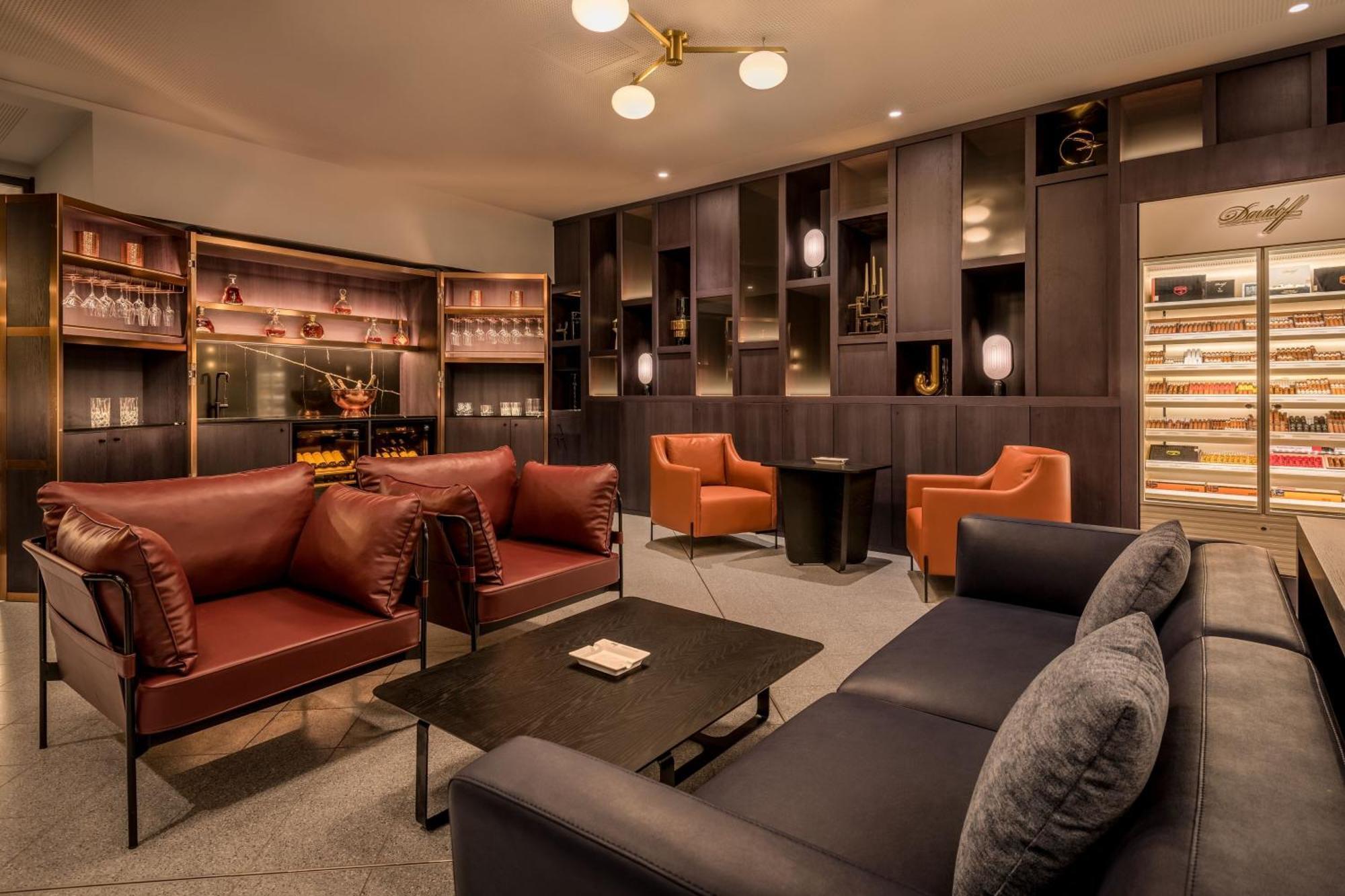 Frankfurt Airport Marriott Hotel فرانكفورت المظهر الخارجي الصورة The photo depicts a stylish and modern lounge area. It features two sets of seating—one composed of two brown leather sofas and a darker blue couch. A black coffee table is situated at the center. There are also two orange armchairs that add a pop of