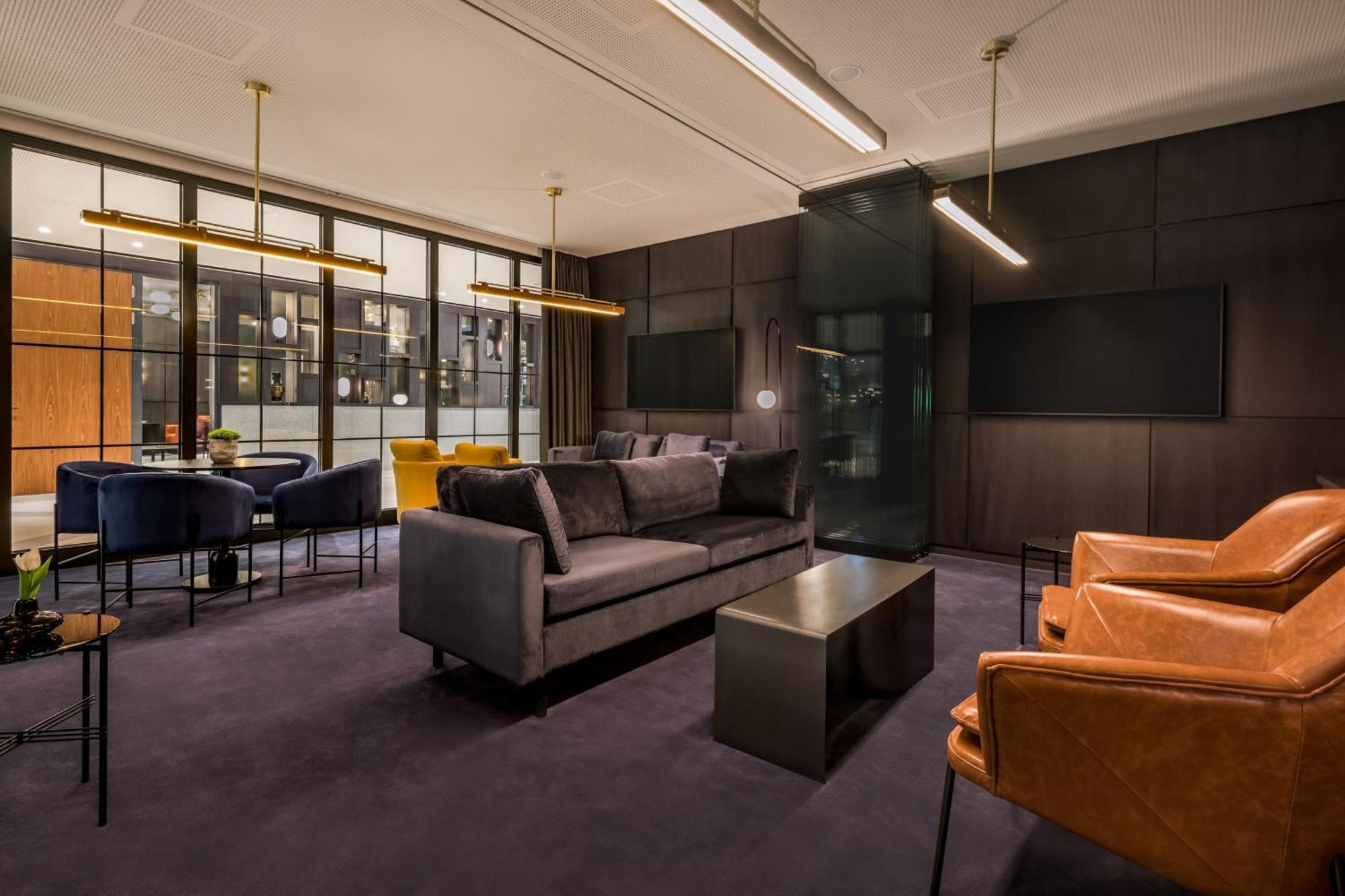 Frankfurt Airport Marriott Hotel فرانكفورت المظهر الخارجي الصورة The photo shows a modern, elegantly designed lounge area. It features a dark-colored sofa in the center, accompanied by brown leather armchairs. There is a sleek, minimalistic coffee table in front of the sofa. Large windows allow natural light to fl