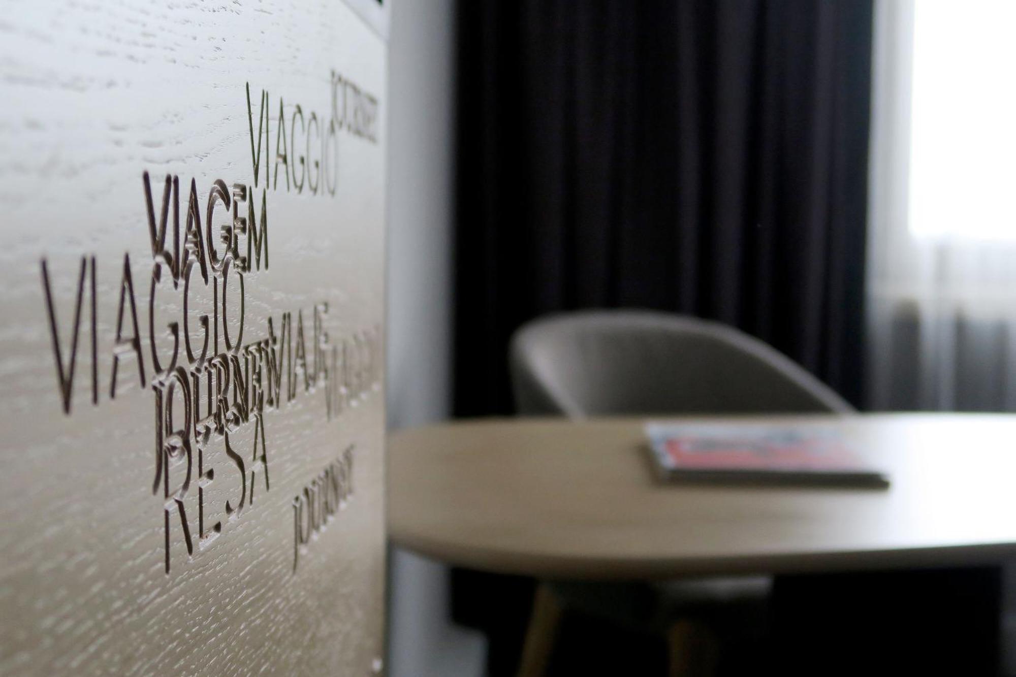 Frankfurt Airport Marriott Hotel فرانكفورت المظهر الخارجي الصورة The photo shows a blurred interior setting, featuring a wall with embossed or engraved words. These words appear to be related to travel or journeys, as one is "VIAGGIO," which translates to "trip" or "journey" in Italian. In the foreground, there is