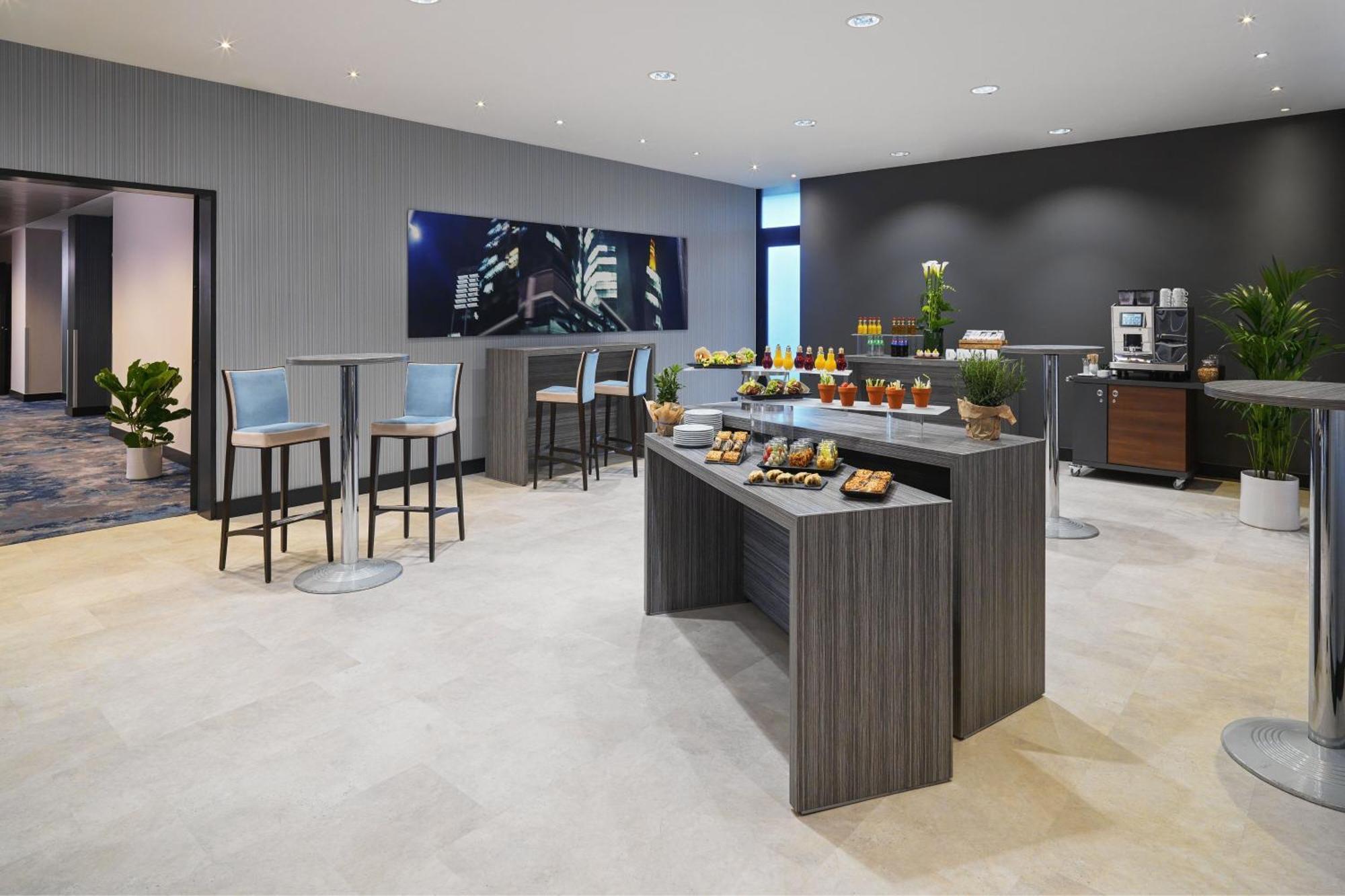 Frankfurt Airport Marriott Hotel فرانكفورت المظهر الخارجي الصورة The photo depicts a modern and stylish lounge area, likely within a hotel or business venue. The space features a combination of seating arrangements, including high tables with stools and a central serving area. 

On the serving table, there are var