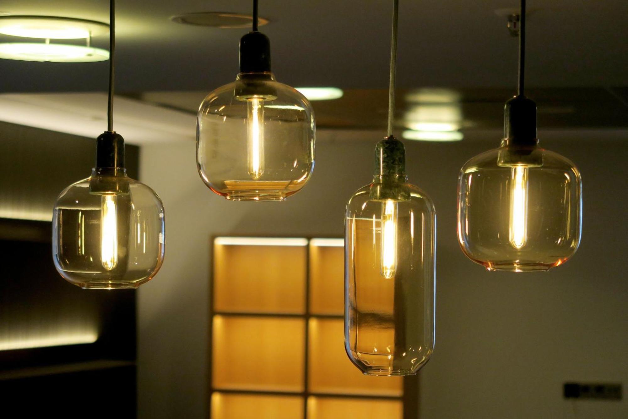 Frankfurt Airport Marriott Hotel فرانكفورت المظهر الخارجي الصورة The photo shows four pendant light fixtures hanging from the ceiling. Each light has a different glass design: two are rounded and two are more cylindrical. The lights are illuminated, casting a warm glow, and they appear to be suspended at varying h