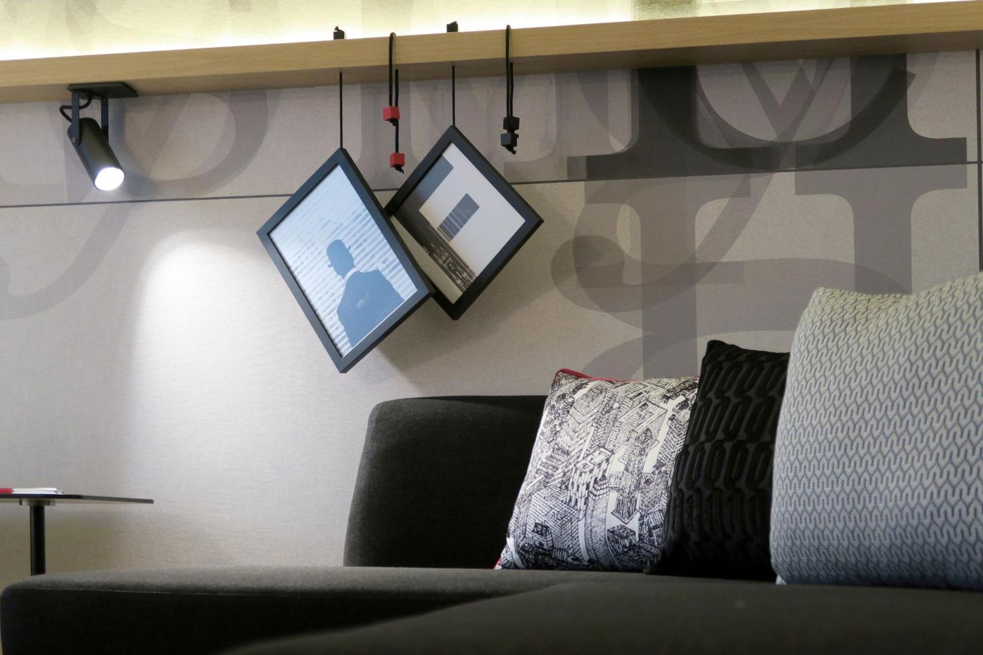Frankfurt Airport Marriott Hotel فرانكفورت المظهر الخارجي الصورة The photo shows a modern interior space, possibly a living room or lounge area. In the foreground, there is a dark-colored sofa with cushions of various textures and patterns. Above the sofa, two frames are suspended at an angle, suggesting a unique 