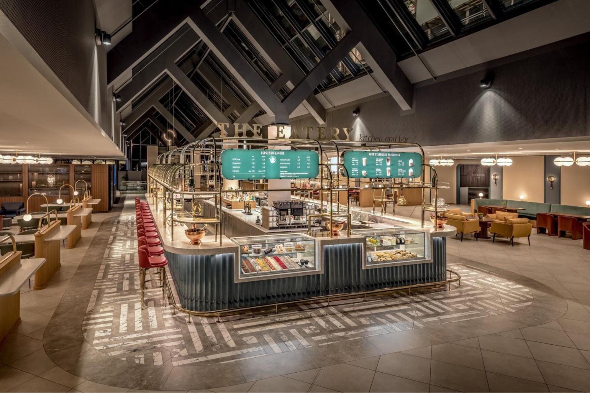 Frankfurt Airport Marriott Hotel فرانكفورت المظهر الخارجي الصورة The photo depicts a modern, stylish restaurant or café interior. The design features a high ceiling with large windows that allow natural light to flood the space. In the center, there is a prominently displayed food counter or bar that showcases var