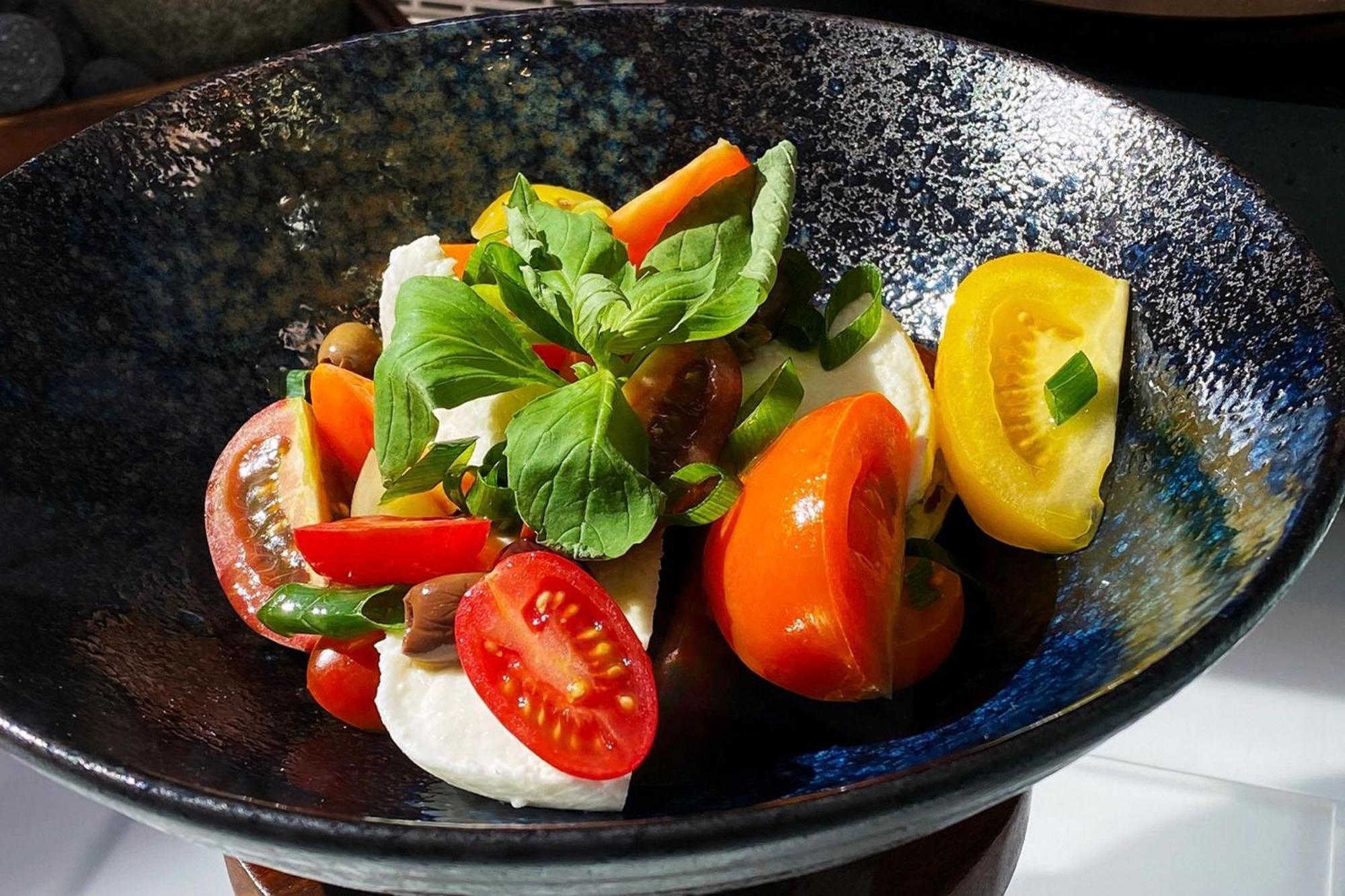 Frankfurt Airport Marriott Hotel فرانكفورت المظهر الخارجي الصورة The photo shows a beautifully arranged salad in a dark, textured bowl. The salad features a variety of colorful vegetables, including sliced yellow and red tomatoes, orange carrot sticks, and fresh green herbs, likely basil. There are also pieces of 