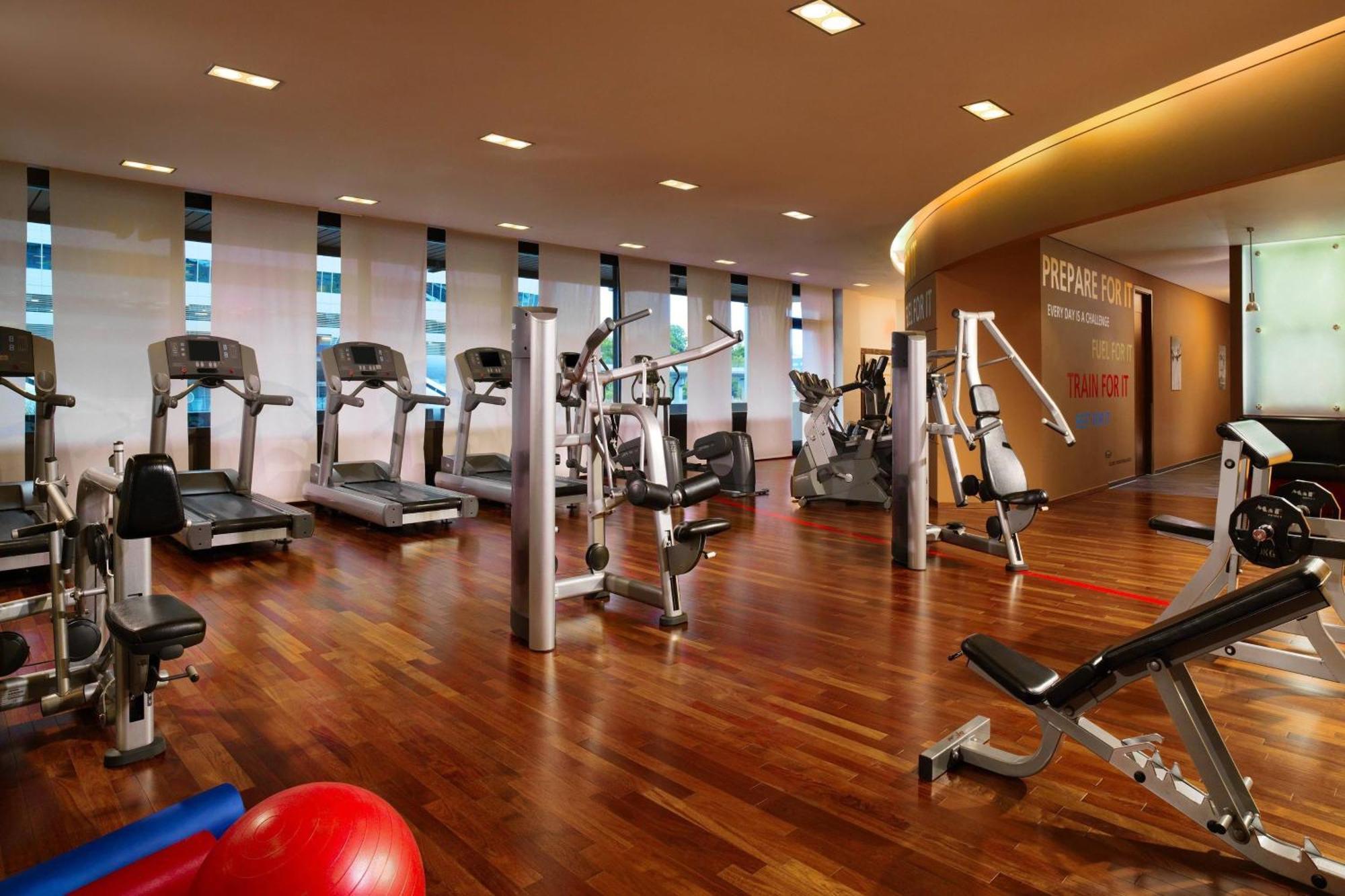 Frankfurt Airport Marriott Hotel فرانكفورت المظهر الخارجي الصورة The photo shows a modern gym or fitness center. It features a variety of exercise equipment including treadmills, weight machines, and free weights. The flooring is made of polished wood, adding a warm tone to the space. Large windows allow natural l