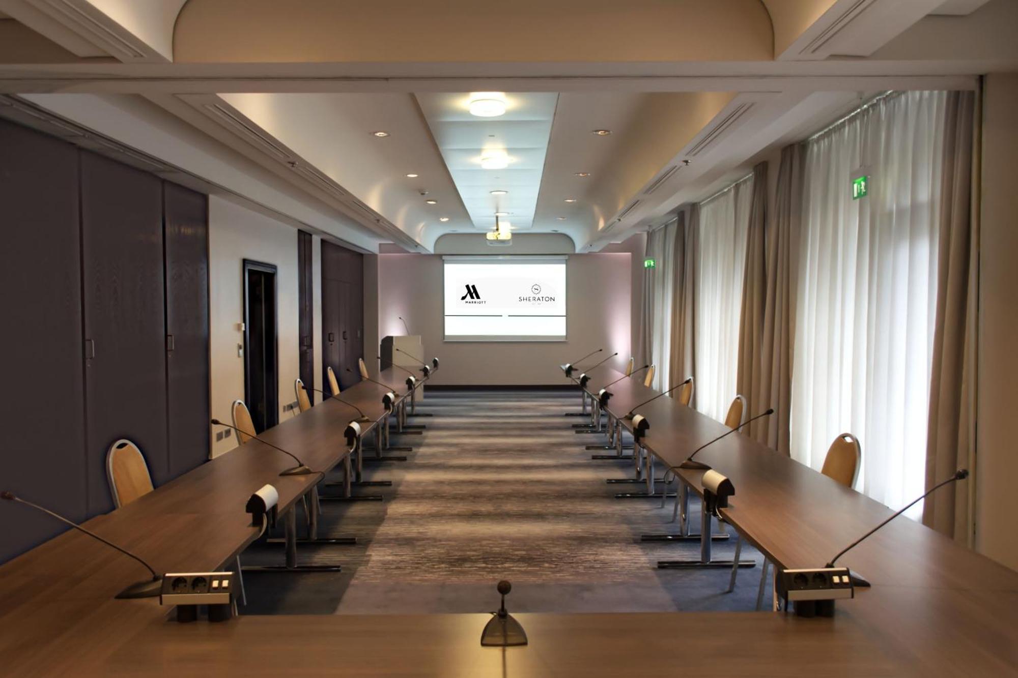 Frankfurt Airport Marriott Hotel فرانكفورت المظهر الخارجي الصورة The photo shows a conference room set up for a meeting. There are two long tables arranged in a U-shape, with chairs positioned around them. The room features a large screen at one end, displaying logos for Marriott and another entity. Soft lighting 